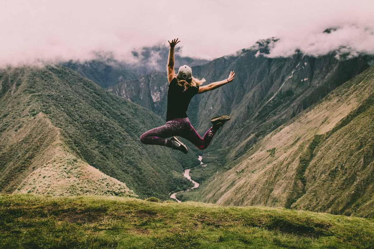 woman jumping in front of green mountain